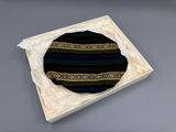 black and green striped hat in a white box on a gray surface