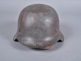 Un vieux casque repose sur une surface blanche, sur fond gris.