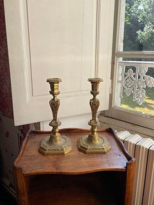 deux bougies dorées posées sur une table en bois près d'une fenêtre
