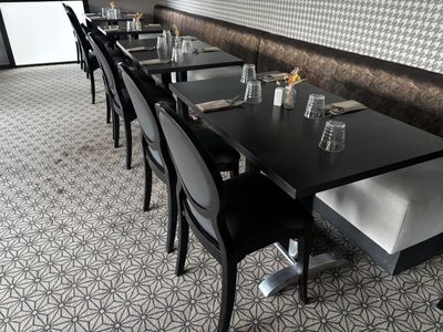 Dans un restaurant dont l'un des murs est recouvert de papier peint, des tables et des chaises sont alignées.