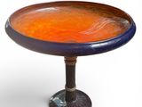an orange and blue glass bowl on a pedestal on a white background