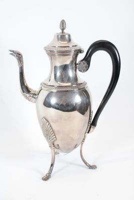 une théière ancienne en argent, dotée d'une anse noire, posée sur un socle