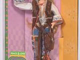 La poupée dans la boîte porte une tenue hippie et tient un gâteau dans les mains