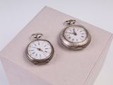 deux montres de poche en argent posées sur un présentoir rose