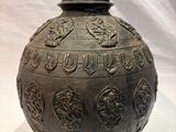 un grand vase en métal muni d'un couvercle, posé sur une surface blanche