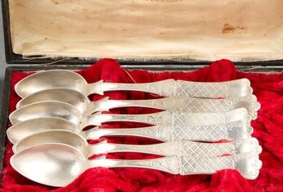cinq cuillères en argent dans un étui posé sur un tissu rouge