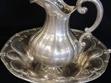 an antique silver plate with a silver pitcher on it on a black background