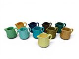 de nombreux pichets de différentes couleurs alignés sur une surface blanche
