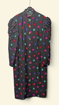 black polka dot dress hanging on a hanger against a white wall