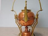 a small copper teapot on a stand on a table