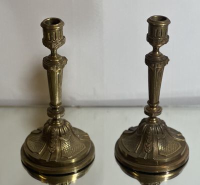 une paire de bougeoirs anciens en laiton posés sur une table en verre, sur fond blanc