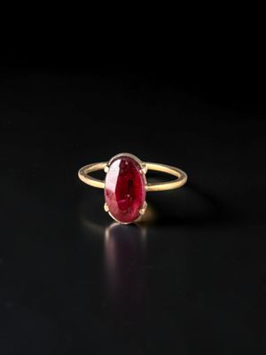 a gold ring with a red stone on a black surface