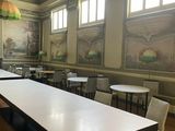 many tables and chairs in a room with a large painting on the wall