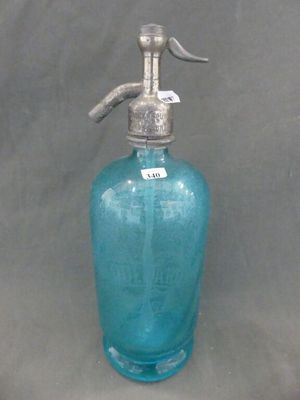 une bouteille en verre bleue munie d'une poignée en métal, sur fond gris