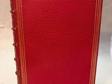 a red book with gold trim sitting on top of a white table