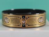 a close up of a black and gold bracelet on a white box