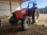un tracteur rouge garé sur la terre battue