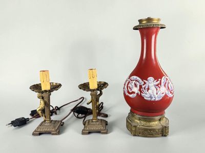 a red vase and two gold candles on a table
