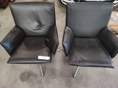 une paire de fauteuils de salon en cuir noir aux pieds chromés, dans un entrepôt