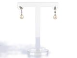 une paire de boucles d'oreilles en perles et diamants, présentée sur un présentoir transparent