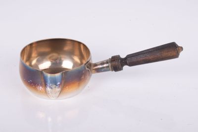 une petite casserole en métal avec un manche en bois posée sur une surface blanche