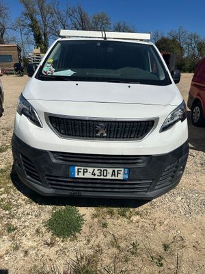 La petite camionnette blanche est garée sur la terre battue, près d'autres voitures.