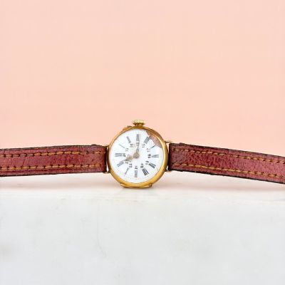 un gros plan d'une montre posée sur une surface blanche, avec un fond rose
