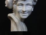 a white marble bust of a woman with a hat on her head