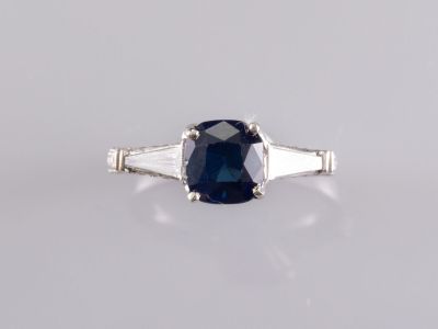 un gros plan d'une bague en saphir et diamants posée sur une surface blanche
