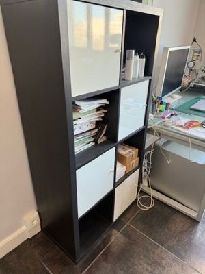 une bibliothèque noire et blanche à côté d'un bureau sur lequel se trouve un ordinateur