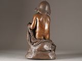 bronze statue of a woman sitting on a rock with a hat on her head