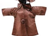 poupée vêtue d'un manteau en cuir marron et d'un chapeau, posée sur un socle noir