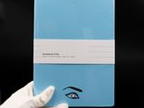 a person in white gloves holding a blue notebook with a blue cover