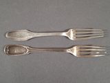 deux fourchettes et une cuillère posées sur une table, sur fond gris