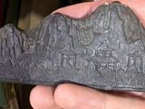 Une personne tient un objet en pierre dans la main, avec une montagne en arrière-plan.