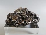 un rocher argenté posé sur un socle transparent, sur une surface blanche