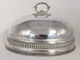 un plat ancien en argent recouvert d'une cloche en verre surmontée d'une couronne