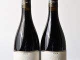 two bottles of red wine sitting on top of a wooden table