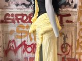 mannequin dressed in yellow and black dress standing in front of graffiti covered wall