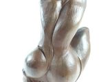 a bronze sculpture of a woman sitting on a white surface