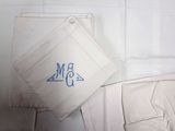 un tissu blanc orné d'un monogramme bleu, à côté d'un pantalon blanc