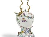 une théière richement décorée, posée sur un socle, sur fond blanc