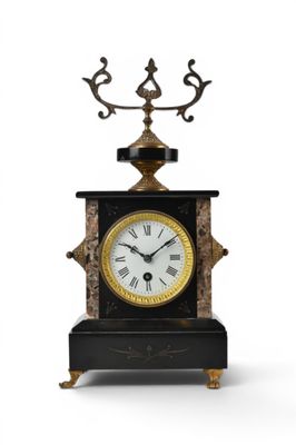 une horloge noire et dorée posée sur un socle, sur fond blanc