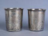 two silver cups with designs on them sitting on top of a table