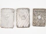 trois étuis à cigarettes en argent posés les uns à côté des autres sur une surface blanche