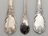 three silver spoons with ornate designs on them sitting next to each other