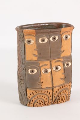 un vase marron orné de visages sur un fond blanc