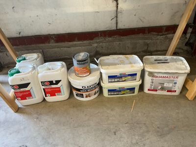 several buckets of paint are lined up on the floor in a garage