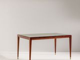 une table avec un plateau en verre et des pieds en laiton dans une pièce blanche