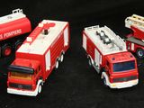 Quatre camions de pompiers miniatures sont alignés en rang sur une surface noire
